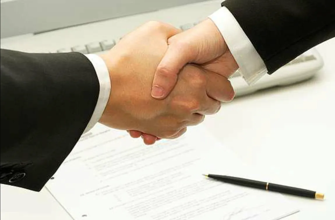 Duas pessoas apertando as mãos sobre contrato assinado, simbolizando acordo comercial ou parceria profissional